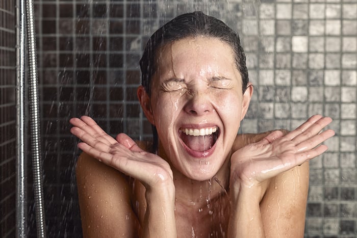 02 Mujer joven sorprendida por la temperatura del agua en la ducha