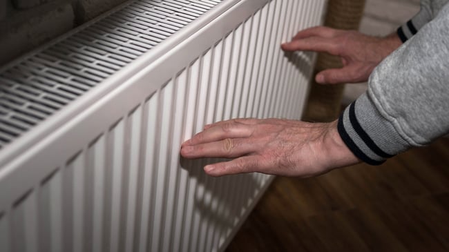 02 Un hombre acerca las manos a un radiador de calefaccion para comprobar la temperatura