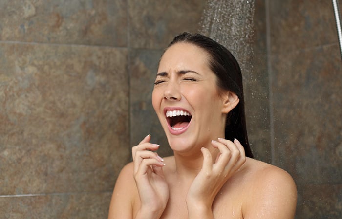 02 Una mujer se sorprende con el agua fria de la ducha porque la esperaba caliente