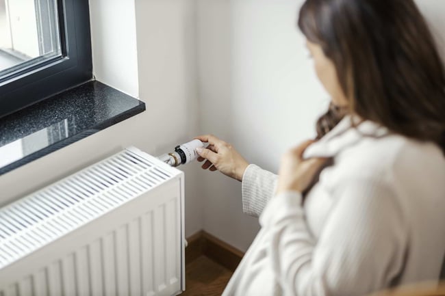 03 Una mujer embarazada aumentando la temperatura de calefaccion en un radiador en su dormitorio