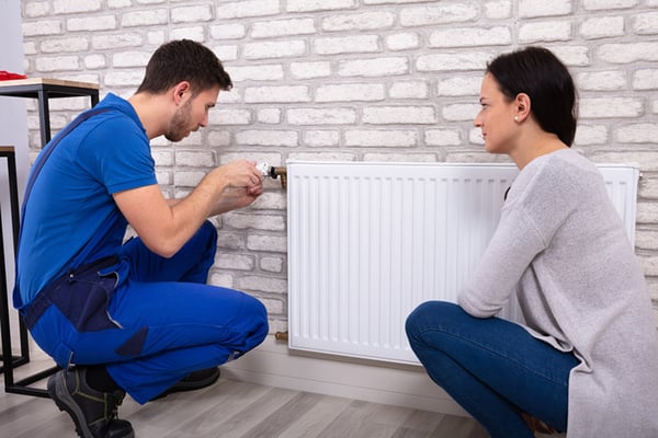 04 Mujer joven mirando mientras un fontanero purga un radiador de calefaccion
