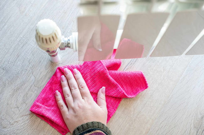 04 Una mano de mujer con un trapo fucsia secando una fuga de agua en un radiador de calefaccion