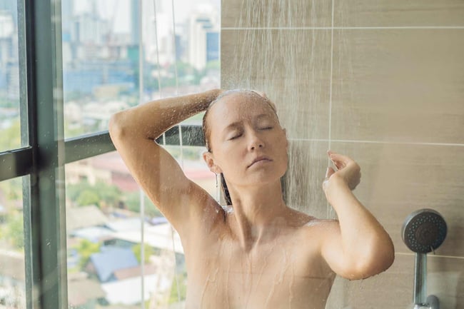 04 Una mujer tomando una ducha caliente junto a una gran ventana de cristal de un edificio