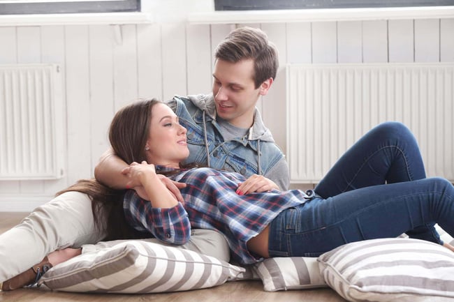 04 Una pareja joven sentada en cojines junto a modernos radiadores de calefaccion de baja temperatura