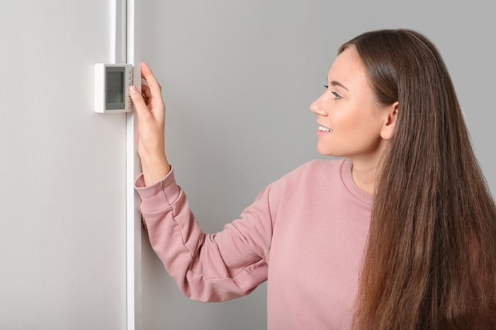 05 Mujer sonriente mientras mira el termostato de la calefaccion