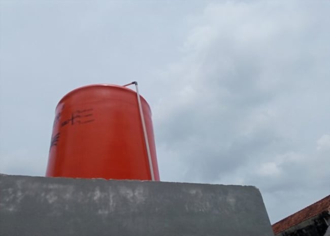 05 Tanque de agua de color rojo oscuro instalado en el tejado de una casa_Plano contra el cielo