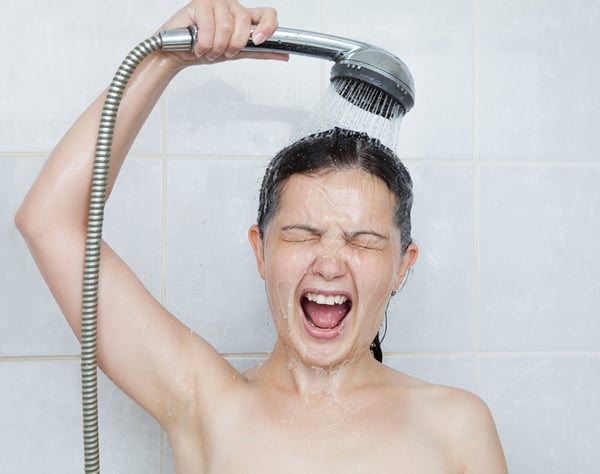 06 Imagen de una mujer joven exclamando porque el agua de la ducha de repente esta fria