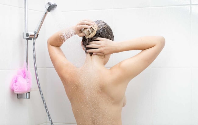 07 Vista trasera de una mujer lavandose el pelo bajo una ducha