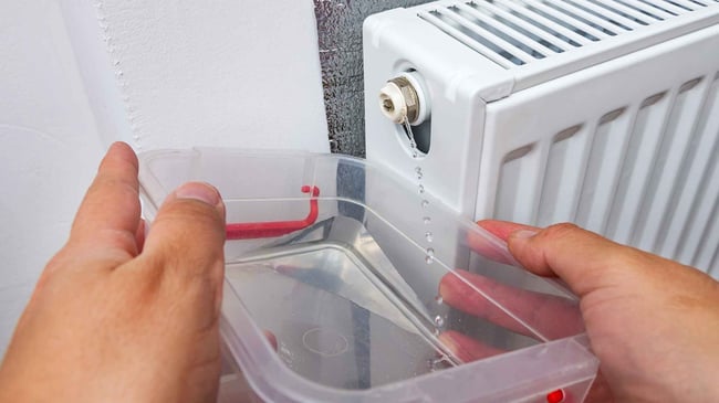 09 Una mano masculina extrayendo agua de un radiador de calefaccion para reducir la presion de la caldera